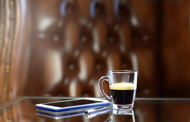 Cup of coffee with the phone on the glass table