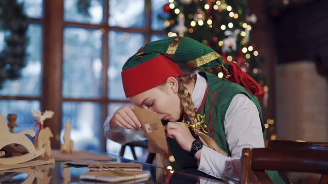Curious elf looking inside the envelope for Santa. Christmas interior cute female elf sits at the table with envelope.