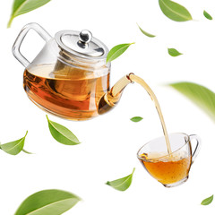 Naklejki  Jug pouring hot tea into glass cup with flying whirl green tea leaves in the air, Healthy products by organic natural ingredients concept, Empty space in studio shot isolated on white background