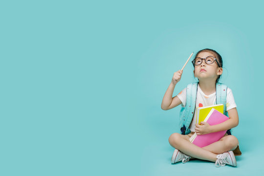 Asian little girl with book thinking and learning, empty space in studio shot isolated on colorful blue background, Creative of baby and genius concept