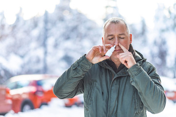 Seasonal cold, runny nose flu virus infection. Mature caucasian man outdoors uses spray drops of medicine in his nose for snot. Allergic renitis and sinusitis.