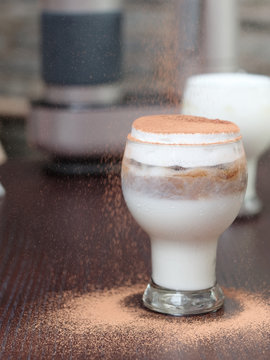 Cup of cold drink made by milk, coffee and cream, covered with coco powder.