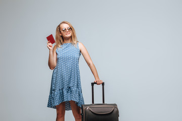 Tourist girl with a suitcase and passport on a gray background