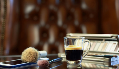 Cup of coffee with the phone and make-up set, shadow palette, and brushes