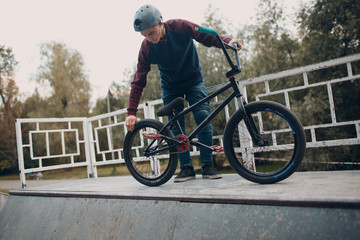 Professional young man sportsman cyclist checking pressure in wheel tires him bmx bike at skatepark