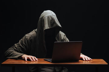 Criminal with laptop in hood on black background