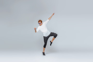 Red-haired man in sunglasses and a white t-shirt dancing on a light background