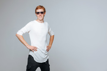 Red-haired man in sunglasses and a white t-shirt posing on a light background