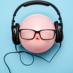 A coral-colored balloon with headphones and glasses on it looks like a funny head.