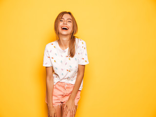Obraz premium Portrait of young beautiful smiling hipster girl in trendy summer jeans shorts clothes. Sexy carefree woman posing near yellow wall in studio. Positive model having fun