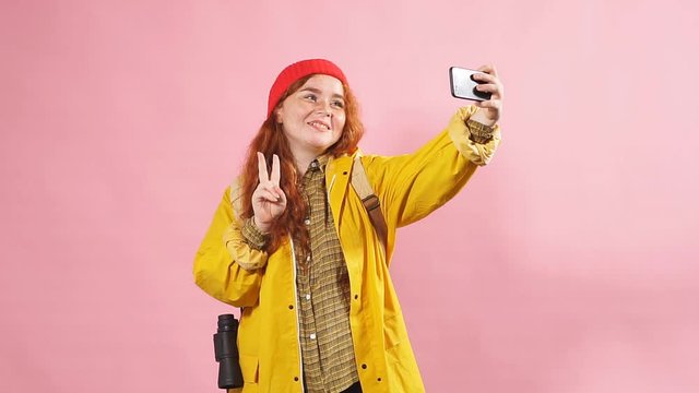 Young happy positive woman in tourist clothes takes a selfie in the Studio