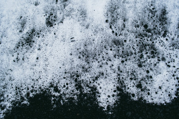 White ocean water foam on the black sand covered with small stones