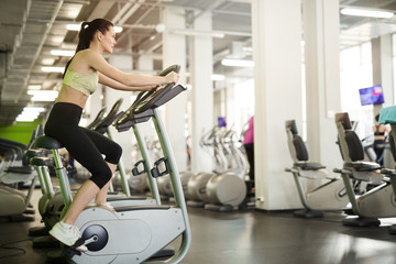 Fototapeta premium Side view portrait of fit young woman on exercise bike enjoying cardio workout alone in empty gym, copy space