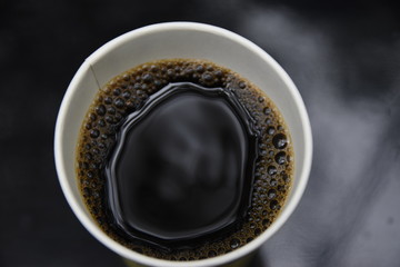 Top view of a paper cup of black brewed coffee on wooden table