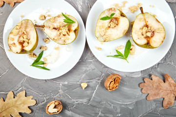 Tasty roast pears with honey and walnuts on white plates on grey background table. Top view.  Flat lay. Copy space.