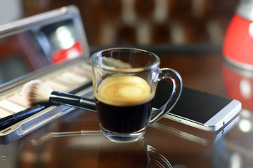 Cup of coffee with the phone and make-up set, shadow palette, and brushes, moka pot coffee