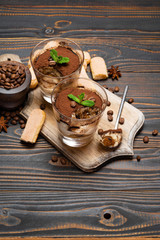 Portion of Classic tiramisu dessert in a glass and savoiardi cookies on wooden background