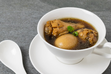 Hard-boiled eggs and chicken in sweet gravy soup in white bowl on tile table.