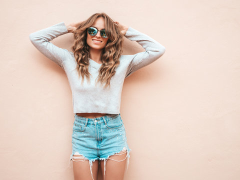 Portrait of beautiful smiling model dressed in summer hipster jeans shorts clothes. Trendy girl posing in the street near wall. Funny and positive woman having fun in sunglasses