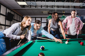 Fototapeta premium Group of young cheerful friends playing billiards.