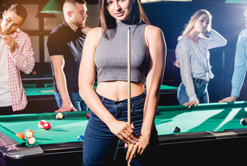 Young woman playing in billiard. Posing near the table with a cue in her hands