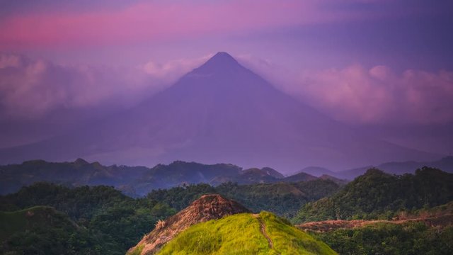 purple dense clouds surround Mayon volcano silhouette among sunny hill in morning time lapse. Concept travel paradise tourism. Exotic nature landscape. Bicol Region Luzon island Philippines. Cinema 4K