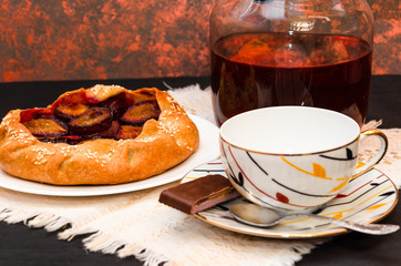 Homemade galette with plums and sesame. Sweet summer fruit pie and white porcelain cup. Vegetarian dessert. Tea party preparation