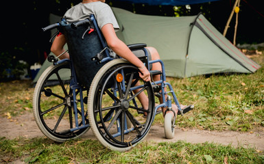 Obraz premium Disabled man resting in a campsite with friends. Wheelchair in the forest on the background of tents