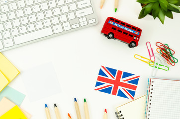 Flat lay frame student desktop with blank spiral notepad, earphones, British bus toy and Britsh flag. Flat lay English learning concept