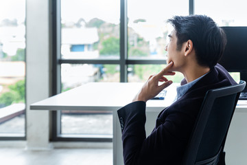 Young Asian businessman Sitting in a modern office is thinking and analyzing to find solutions to improve business performance