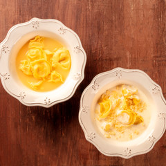 Tortellini with broth and cream sauce, Italian food, overhead square shot on a dark rustic wooden background with a place for text