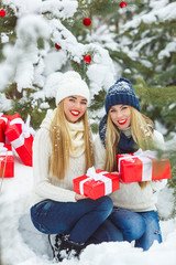 Girlfriends having fun with Christmas presents outdoors. Women holding gifts. Ladies holding red boxes on winter background