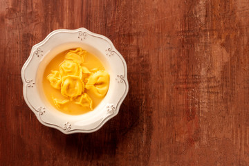 Tortellini with broth, shot from above on a dark rustic wooden background with copyspace