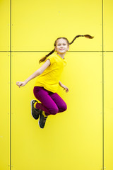 Young girl having fun and jumping high. Smiling girl with yellow background wearing a yellow t-shirt and purple pants