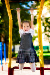 Fototapeta premium Girl schoolgirl in a school uniform climbs a sports horizontal bar