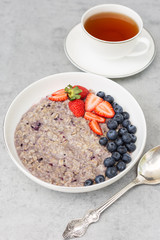 Blueberry oat porridge with strawberry, close up on gray background