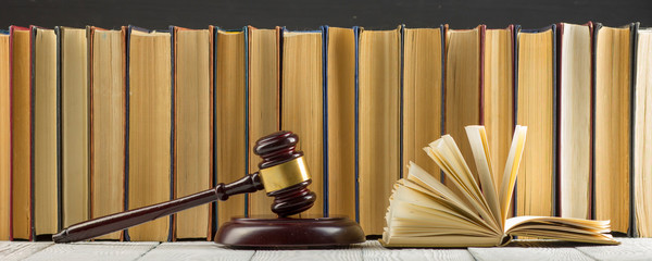 Legal Law concept - Open law book with a wooden judges gavel on table in a courtroom or law...