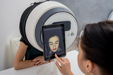 Face skin analyze system. Cosmetologist analyzing woman face. Modern technologies.