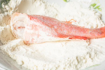 Fresh sea bass rolled in white flour for frying in pan.