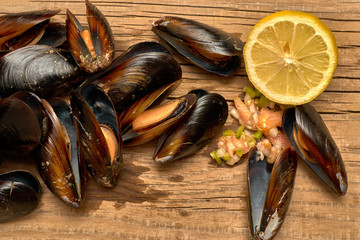 Mejillones al vapor abiertos enteros con limón y picadillo de verdura sobre una mesa de madera