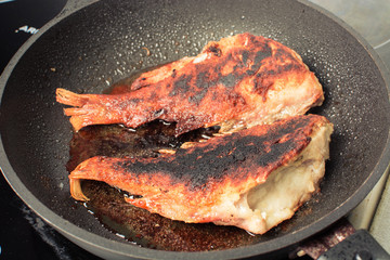 Red sea bass is fried in frying pan on stove.