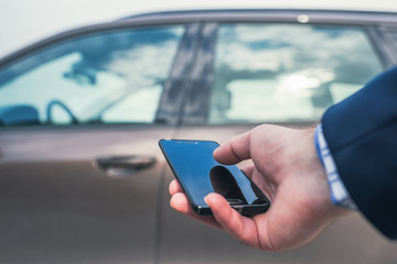Customer hand holding mobile phone for opening car door. Car sharing service or rental concept.