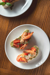 bruschetta with shrimp, basilб pesto sauce and mozzarella on a white plate on a wooden background. Italian restaurant. Top view food photo