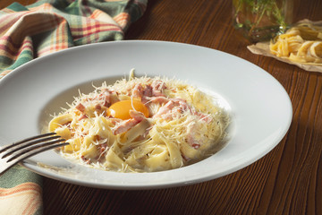 Carbonara pasta with raw yolk, parmesan, white sauce, bacon on wooden background. Selective focus, close up. Italian cuisine food photo background
