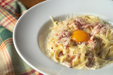 Carbonara pasta with raw yolk, parmesan, white sauce, bacon on wooden background. Selective focus, close up. Italian cuisine food photo background