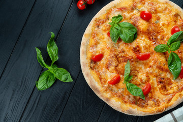Homemade fresh Pizza Margherita with red sauce, basil and cherry tomato on a black wooden with copy space. Top view food photo. Flat lay. Italian cuisine.