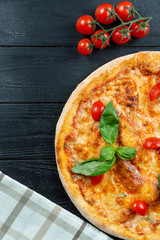 Homemade fresh Pizza Margherita with red sauce, basil and cherry tomato on a black wooden with copy space. Top view food photo. Flat lay. Italian cuisine.