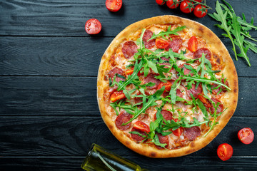 Homemade fresh Pizza with salami, cherry tomatoes and arugula on a black wooden with copy space. Top view food photo. Flat lay. Italian cuisine.