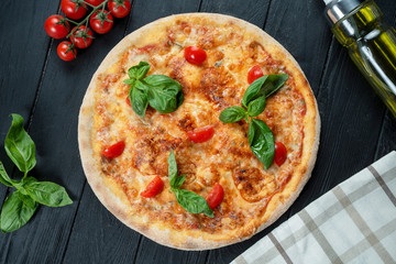 Homemade fresh Pizza Margherita with red sauce, basil and cherry tomato on a black wooden with copy space. Top view food photo. Flat lay. Italian cuisine.