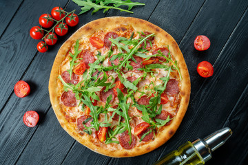 Homemade fresh Pizza with salami, cherry tomatoes and arugula on a black wooden with copy space. Top view food photo. Flat lay. Italian cuisine.